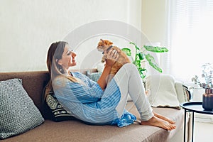 Playing with cat at home. Young woman sitting on couch and hugging pet