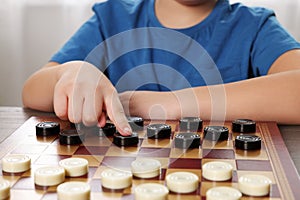 Playing checkers. Boy thinking about next move at table in room, closeup