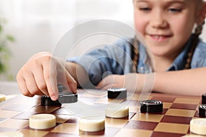 Playing checkers. Little girl thinking about next move at table in room, closeup