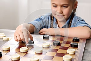 Playing checkers. Little girl thinking about next move at table in room, closeup