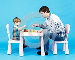 Playing chess with dad - little boy and his father on blue