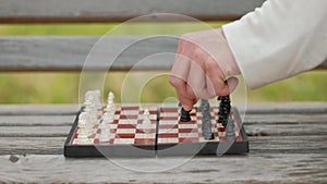 Playing chess outdoor. Chess board and figures on the bench, against the backdrop of greenery. Close-up.