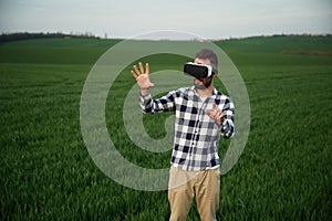 Playing game in VR glasses. Handsome young man is on agricultural field