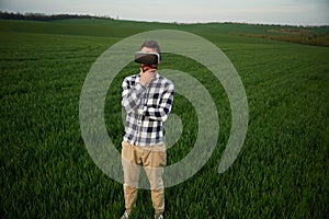 Playing game in VR glasses. Handsome young man is on agricultural field