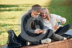 Playing games by using smartphones. Two young students are together outdoors