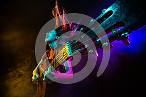 Playing guitar. Young woman with smoke and neon light on black background. Highly tensioned, wide angle, fish eye view
