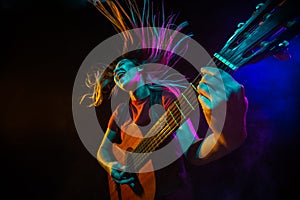 Playing guitar. Young woman with smoke and neon light on black background. Highly tensioned, wide angle, fish eye view