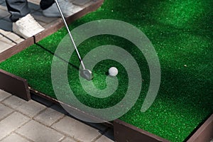 Playing in mini-golf on the green grass using niblick. Player hits white ball. Golf sport game. Advert for golf club.