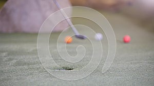 Playing mini golf. A person hitting several golf balls in a row and misses