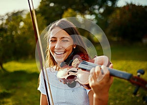 Playing with nature all around always makes her happy. a young girl playing a violin outdoors.