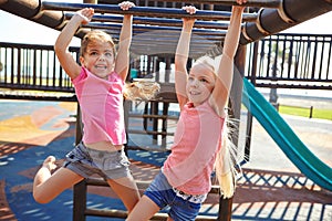 Playing outside makes them happier, healthier and smarter. two little girls hanging on the monkey bars at the playground