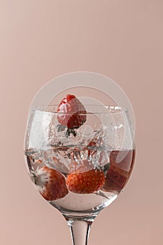 playing with strawberries in a glass with transparent liquid, uniform salmon color background