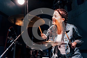 Plays drums. Young beautiful female performer rehearsing in a recording studio