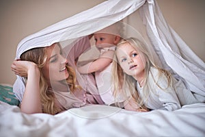 Playtime shenanigans with the girls. Shot of an adorable family of three playing under a sheet on the bed at home.