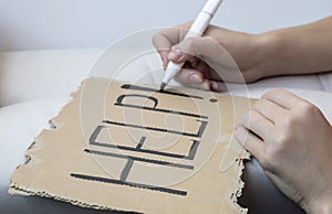 A plea for help. A woman writes the word help on a sheet of cardboard