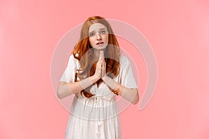Pleading cute and silly redhead girl acting innocent, press hands together in pray, asking for favour, hopefully looking