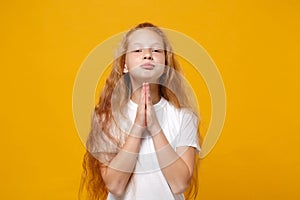 Pleading little ginger kid girl 12-13 years old in white t-shirt isolated on yellow wall background children portrait