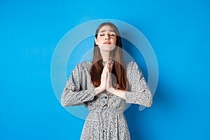 Pleading woman in dress begging for wish come true, supplicating god, standing against blue background