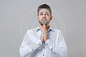 Pleading young unshaven business man in light shirt posing isolated on grey wall background. Achievement career wealth