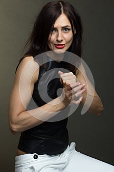 Pleas do not a brunette in a black leather sleeveless blouse and white trousers poses on a gray background