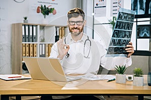 Pleasant 35-aged man scientist sitting at desk with x ray scan in hands