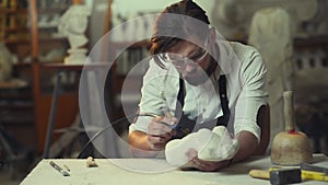 Pleasant attentive handsome modern bearded sculptor grinding stone sculpture in his creative workshop. Young man working