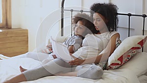 Pleasant biracial woman reading book to daughter.