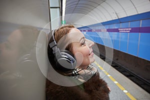 A pleasant blonde 35-40 years old inside the subway listens to music through high-quality over-ear headphones connected