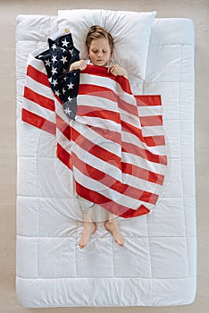 Pleasant blonde boy being covered with the US flag