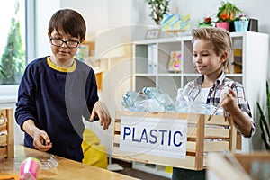 Pleasant blonde boy carrying box with plastic bottle after sorting