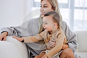 pleasant blonde female hugging little boy son and looking at side together