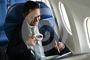 Pleasant businessman passenger checking news on digital tablet, using wireless connection on board during flight