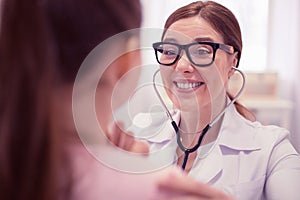 Pleasant cheerful general practitioner wearing glasses examining cute girl