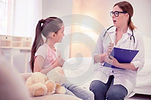 Pleasant dark-haired family physician consulting cute little girl