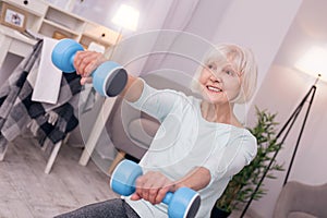 Pleasant elderly woman holding blue dumbbells and smiling