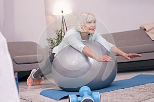 Pleasant elderly woman lying on exercise ball