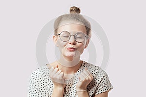Pleasant girl with hairbun and glasses blowing sweet kiss.