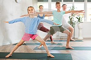 Pleasant little girl practicing warrior pose of yoga with her family