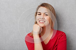 Pleasant looking pleased female has pleasant smile, demonstrates white perfect teeth, keeps hand under chin, being glad to be phot