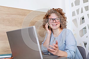 Pleasant looking successful professional female lawyer/business woman talking on the mobile phone, works on laptop computer,