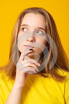 Pleasant looking teen girl holds chin and looks pensive away, thinks about great plan, has new ideas in mind