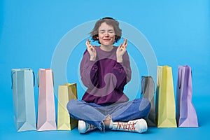 Pleasant looking young lovely short haired curly female raising hands with crossed fingers and smiling hopefully with closed eyes