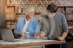 Pleasant mentor helping young colleague draw blueprint