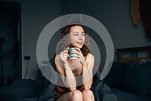 Pleasant middle-aged girl in bed wrapped in a blanket with a mug