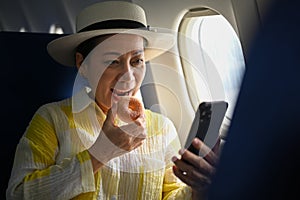 Pleasant middle aged woman eating donut and using smart phone, waiting for airplane taking off from the airport