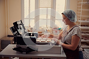 Pleasant middle-aged woman in the process of printing images on gingerbread with food coloring. Small wholesale