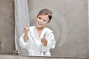 Pleasant nice child boy showing thumbs up after cleaning, shaving, smiling satisfied