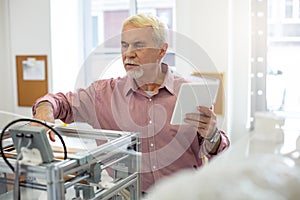 Pleasant senior man changing 3D printer configurations photo