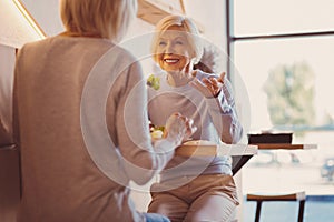 Pleasant senior women chatting and laughing while eating out