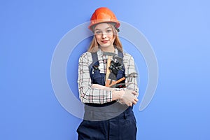 Pleasant service woman wearing orange helmet and blue coverall holding wrench, hammer and other tools